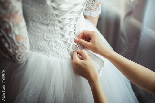 Bridesmaid makes bow-knot on the back of brides wedding dress