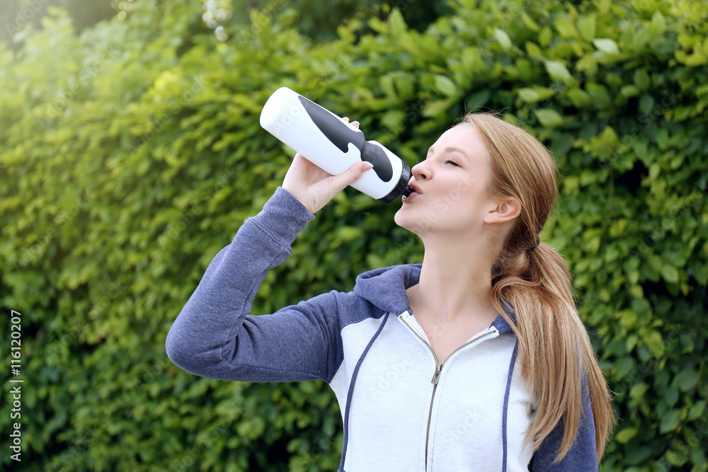 Sporty woman drinking water after jogging at park on a sunny day Sporty woman drinking water after jogging at park on a sunny day