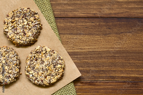 Vegane Plätzchen aus Bananen, Haferflocken, gerösteten Haferkörner, Leinsamen, Mohnen, Kokosraspeln, Chia Samen und Zimtpulver, fotografiert auf dunklem Holz mit natürlichem Licht photo