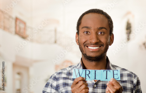 Headshot handsome man holding up small letters spelling the word write and smiling to camera