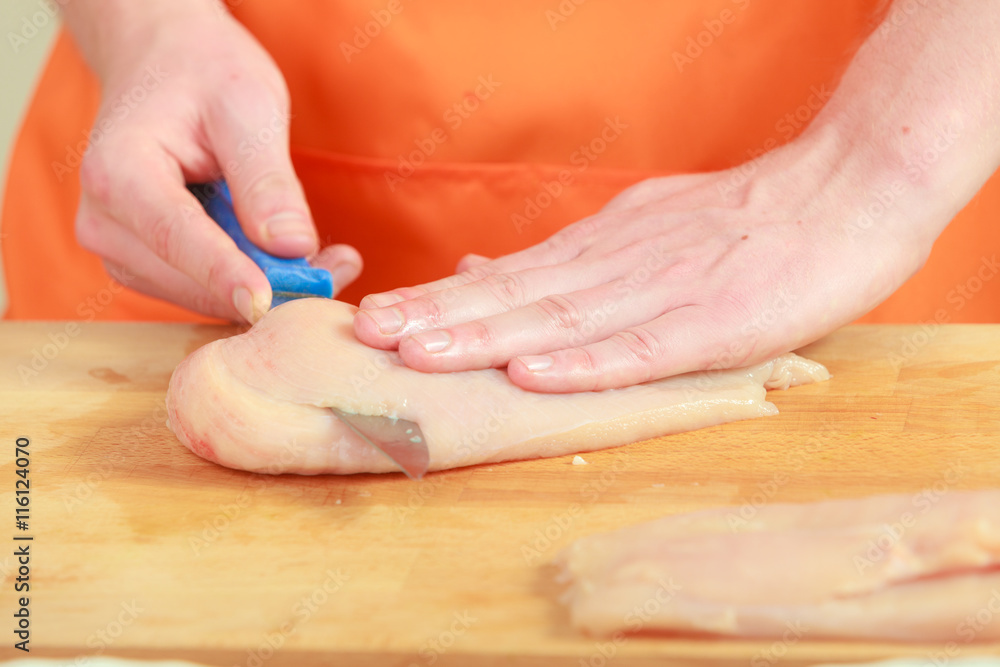 Man cutting raw chicken meat on wooden board Man cutting raw chicken meat on wooden board