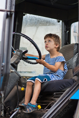 маленький мальчик сидит в кабине трактора. Мальчик крутит руль