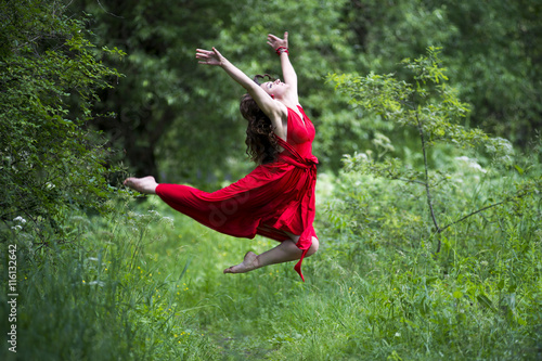 Happy beautiful young caucasian brunette woman in red dress jumping outdoors