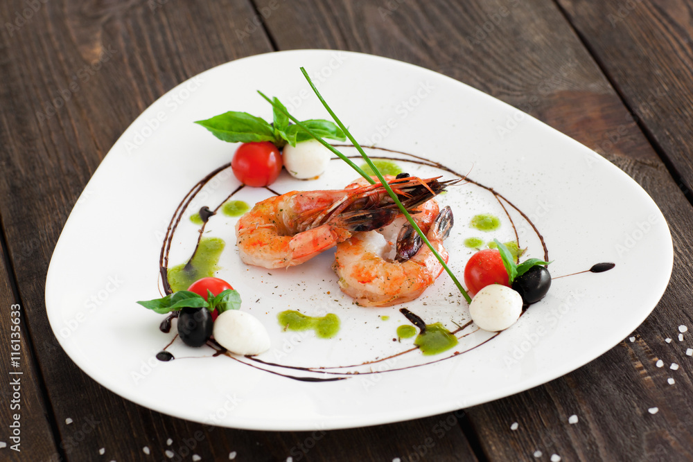 Grilled shrimps on white triangle plate on wooden background, served with olives, cherry tomato and mozzarella cheese