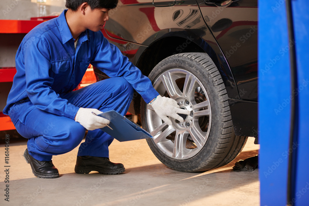 Young Vietnamese auto mechanic checking tyre in garage Young Vietnamese auto mechanic checking tyre in garage