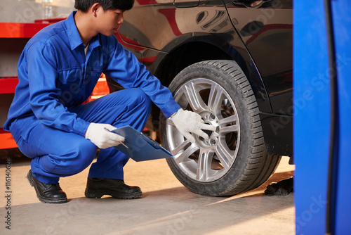 Young Vietnamese auto mechanic checking tyre in garage © DragonImages