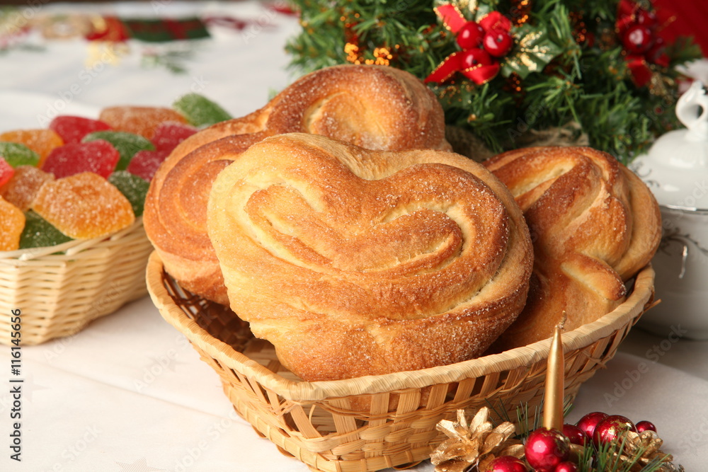 close-up of sweet rolls in the shape of hearts in a wicker basket and Christmas decorations on a white tablecloth in the studio