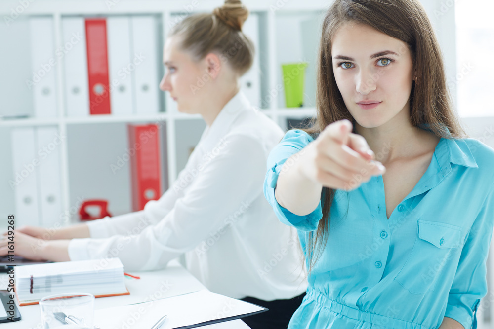 .Portrait of young businesswoman pointing straight to the camera, with female colleague on the background. .Portrait of young businesswoman pointing straight to the camera, with female colleague on the background.