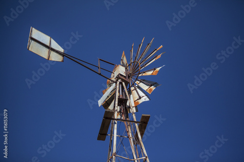 Disused rusty old farm windmill against blue sky