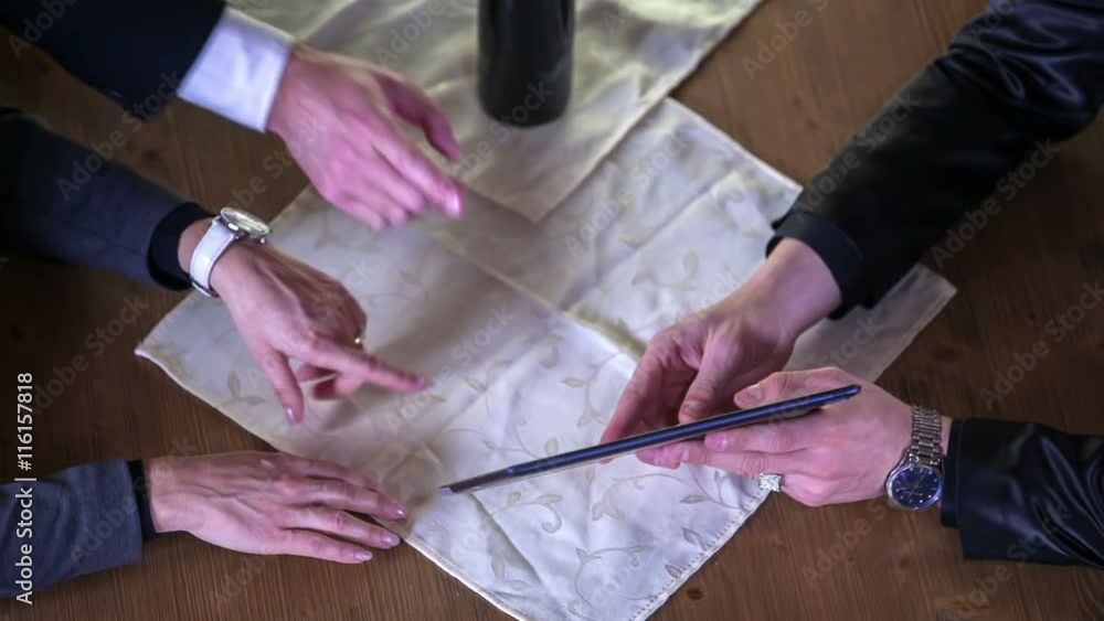 Four people are having a business meeting, a tablet is in front of them and they're talking about different options. Close-up shot.
