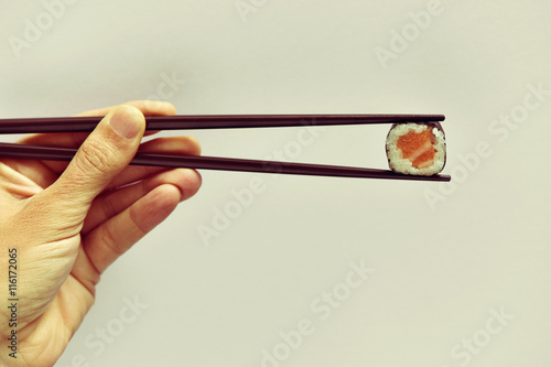 young man picking a makizushi with a pair of chopsticks