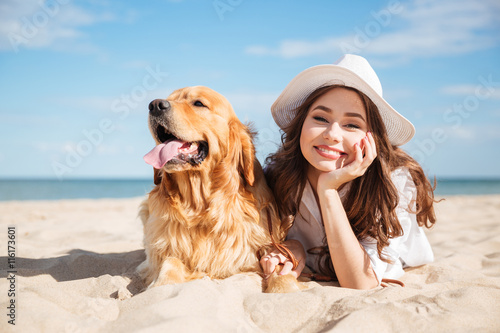 Canvas Print Cheerful young woman lying with her dog on the beach