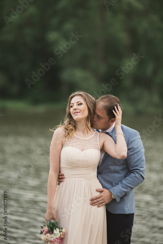 Beautiful wedding couple, bride,groom kissing and posing on the bridge near lake © olegparylyak
