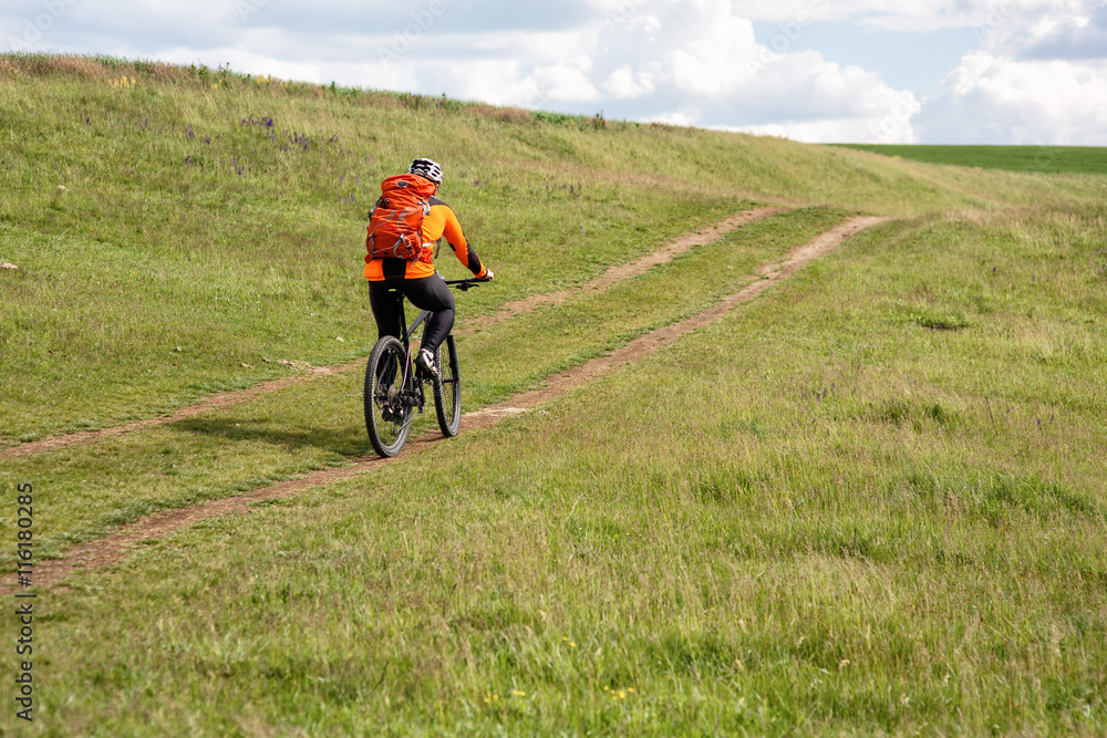 Young man cycling on a rural road through green meadow Young man cycling on a rural road through green meadow