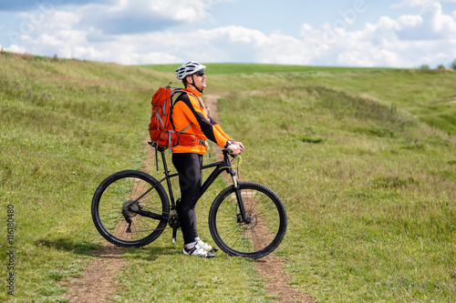 Young man cycling on a rural road through green meadow