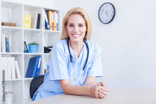 Beautiful blonde female doctor sitting at office desk working. Health care and prevention concept