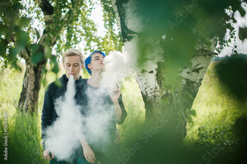 young couple with dyed hair smoking electronic cigarettes near birches. cloud head. cloud chasing photo