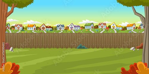 Wood fence on the backyard of a colorful house in suburb neighborhood. Green garden with grass, trees, flowers and clouds.
