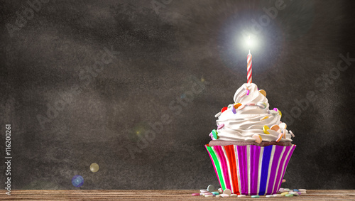 Obraz na płótnie Cupcake à la crème, bonbons et une bougie sur une table en bois sur fond de tableau noir