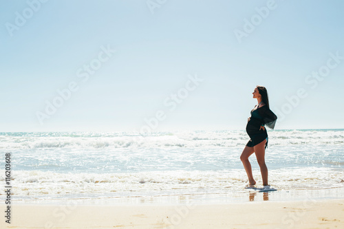 Silhouette of a pregnant woman on sea background. Expectant mother enjoys sea views. Beautiful pregnant woman standing on the beach