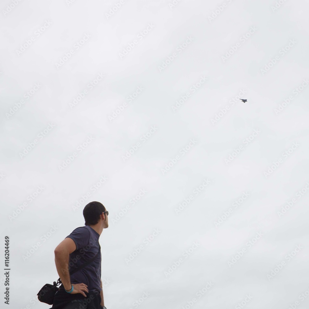 guy looking up to a fighter plane in the cloudy sky
