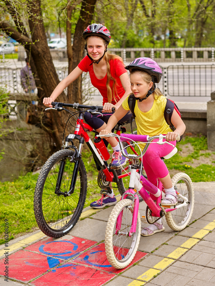 Fototapeta premium Children girls wearing bicycle helmet with rucksack ciclyng bicycle. Girls children cycling on yellow bike lane. Bike share program save money and time. City trip.