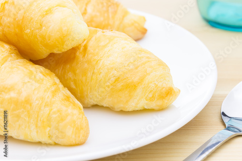 Croissant or bread on white dish on wood table and glass and spoon