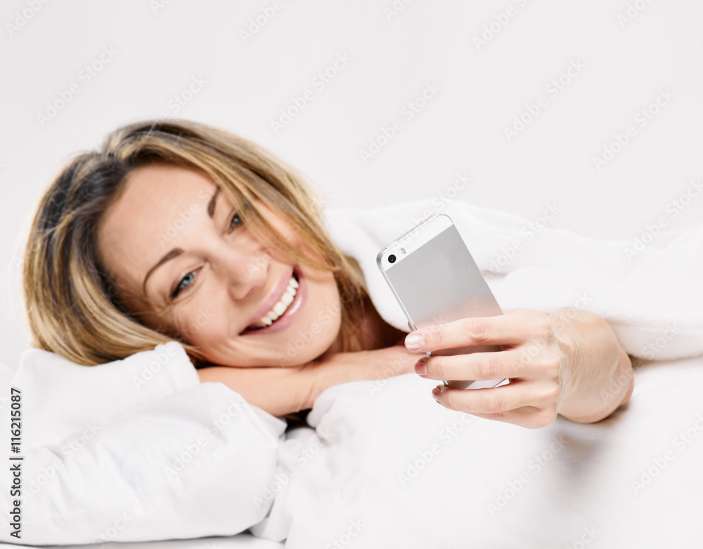 woman lying on bed smiling, reading a text message woman lying on bed smiling, reading a text message