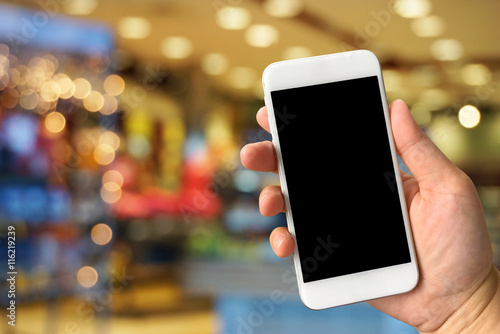 Woman hand holding smartphone against blur bokeh of shop backgro