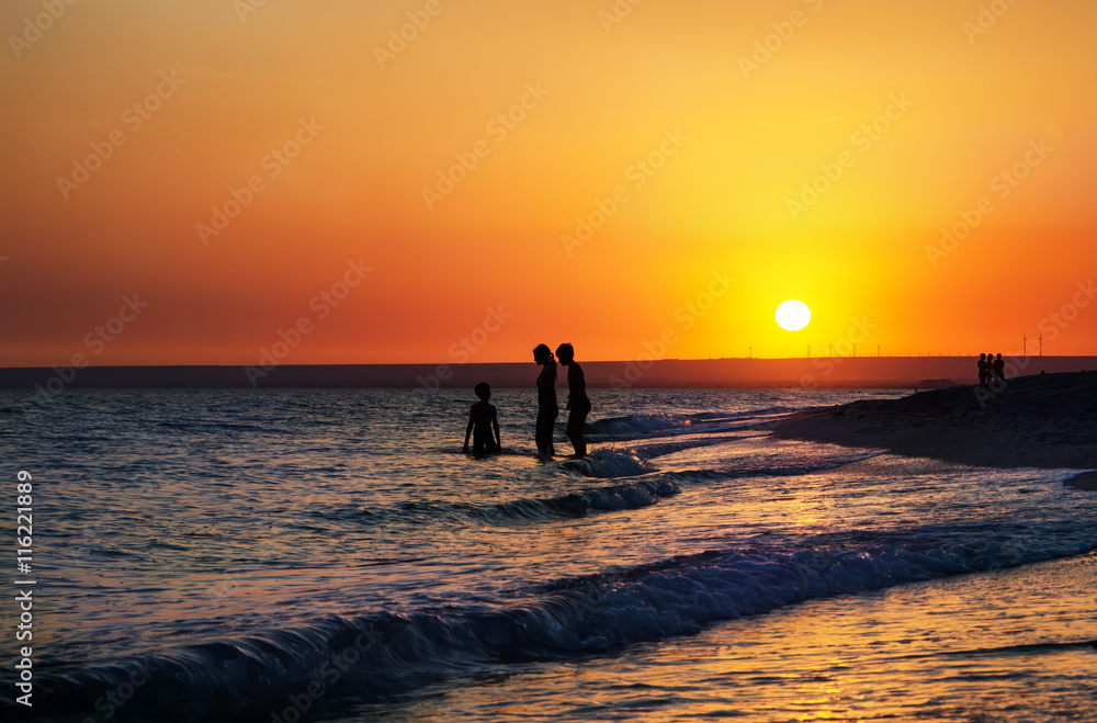 Silhouettes of people in the sea at sunset background