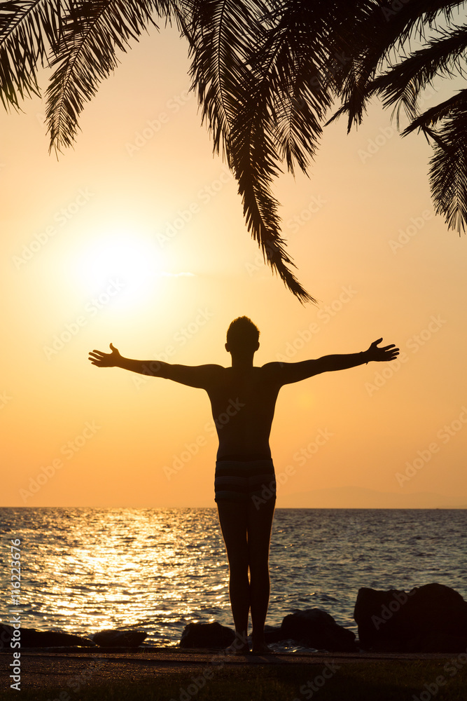 Silhouette of man raised his hands to the sky at sunset