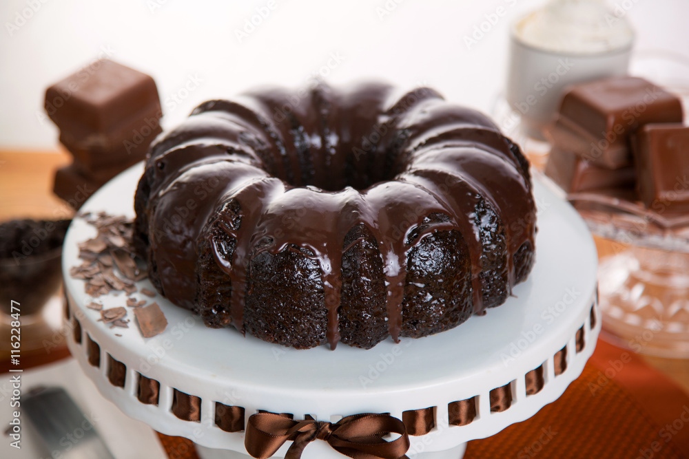Thick rich chocolate bundt cake with dripping fudge sauce on a cake stand