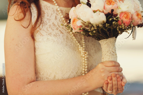 Bride in pearls holds a wedding bouquet decotated with lace photo