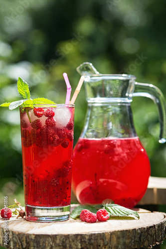 Homemade berry juice in a glass and jug with raspberry redcurrant in summer garden