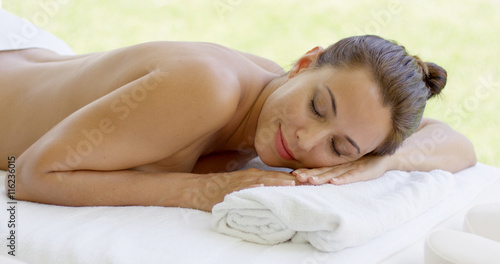 Woman relaxing on spa table on outdoor patio closes her eyes and smiles to herself