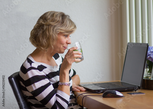 Foto Attractive middle-aged woman looking at the monitor and drinking