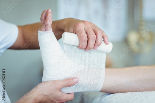 Tableau sur toile Physiotherapist putting bandage on injured feet of patient