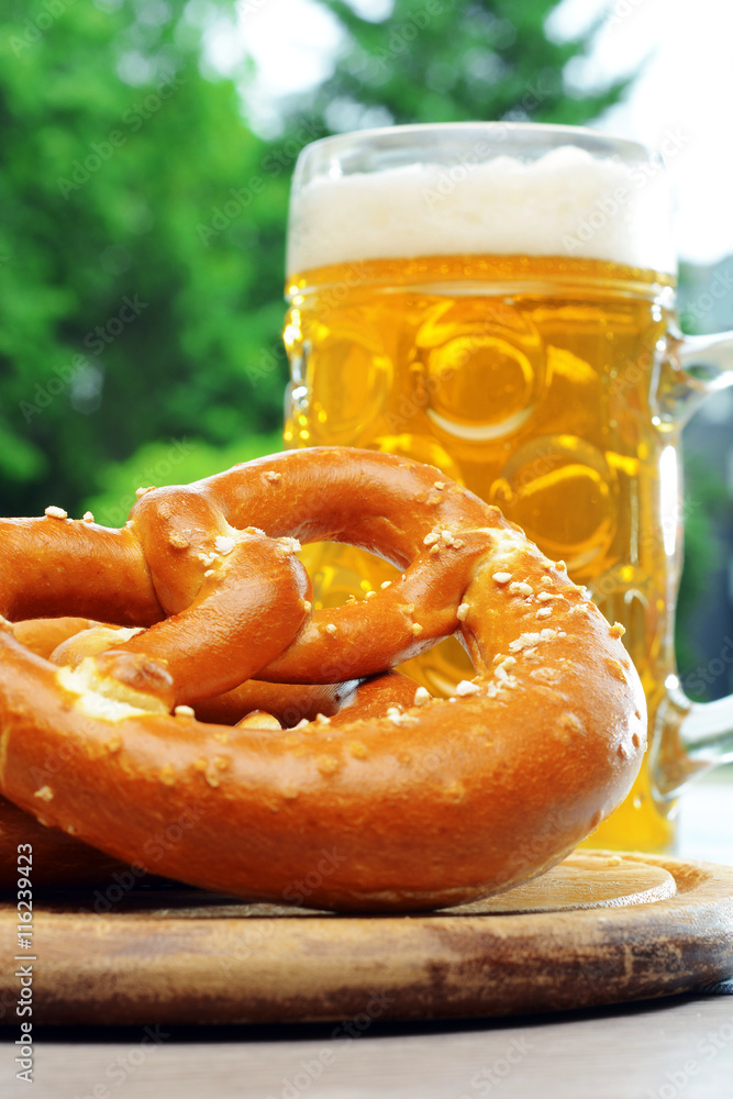 Brezel, Salzbrezel, Laugenbrezel oder Brezn mit Maß Bier auf Tisch im Biergarten zum Oktoberfest Brezel, Salzbrezel, Laugenbrezel oder Brezn mit Maß Bier auf Tisch im Biergarten zum Oktoberfest