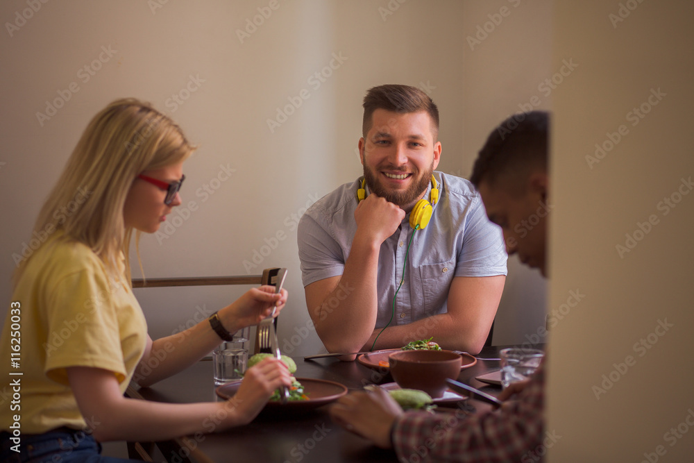 Fototapeta premium Happy friends spending their free time in vegan restaurant or cafe. Smiling man looking at camera while his friends eating healthy vegan dishes.