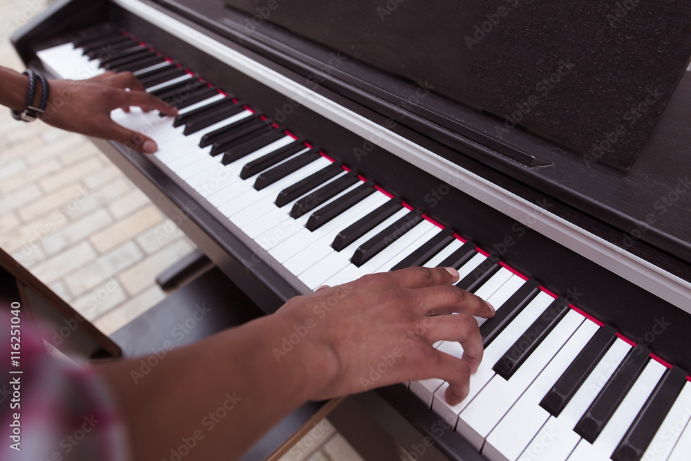 Closeup picture of of keyboard of piano. Black man playing piano outdoors in city centre. Professional musician playing piano. Closeup picture of of keyboard of piano. Black man playing piano outdoors in city centre. Professional musician playing piano.