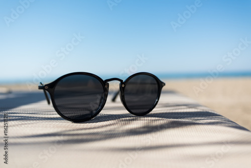 Fototapeta Naklejka Na Ścianę i Meble -  Female sunglasses on a sun lounger with defocused sand beach and sea on the background