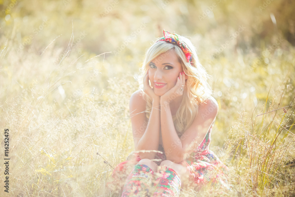 beautiful girl relaxing lying on the grass in the field. Embracing blond woman. Flowers textile bandana. wild summer flowers around. Embracing fashion advertising model. Woman in red dress and boots beautiful girl relaxing lying on the grass in the field. Embracing blond woman. Flowers textile bandana. wild summer flowers around. Embracing fashion advertising model. Woman in red dress and boots