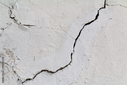 Фотография Crack. Texture of old painted white plaster. Cracked wall.