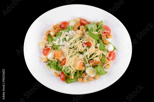 Caesar salad with prawns, cherry tomato and cheese on white plate on black background