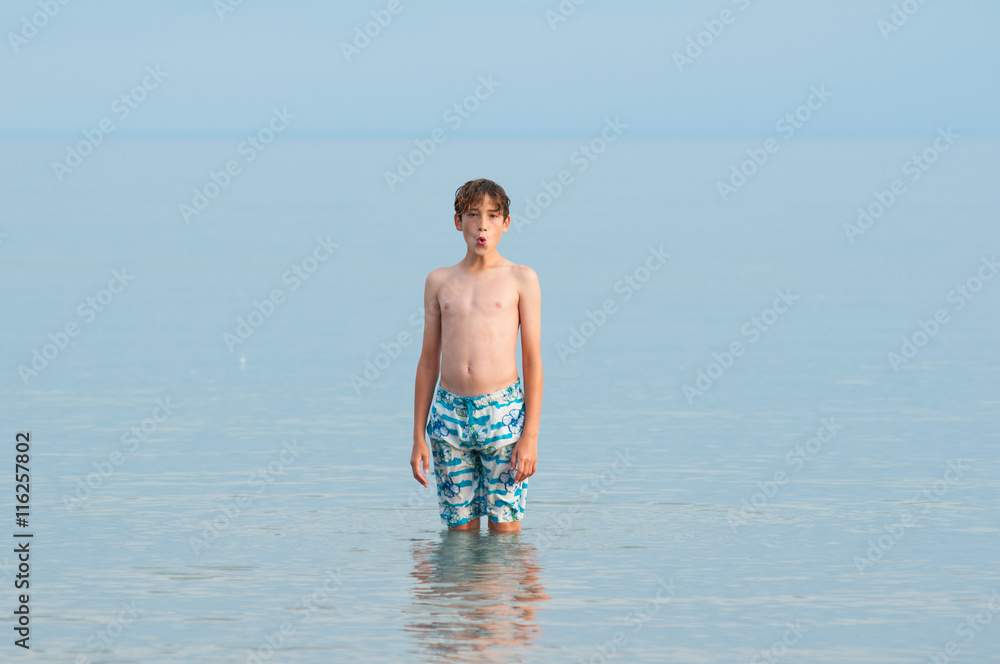 single child standing in a calm blue grey lake in his bathing suit single child standing in a calm blue grey lake in his bathing suit