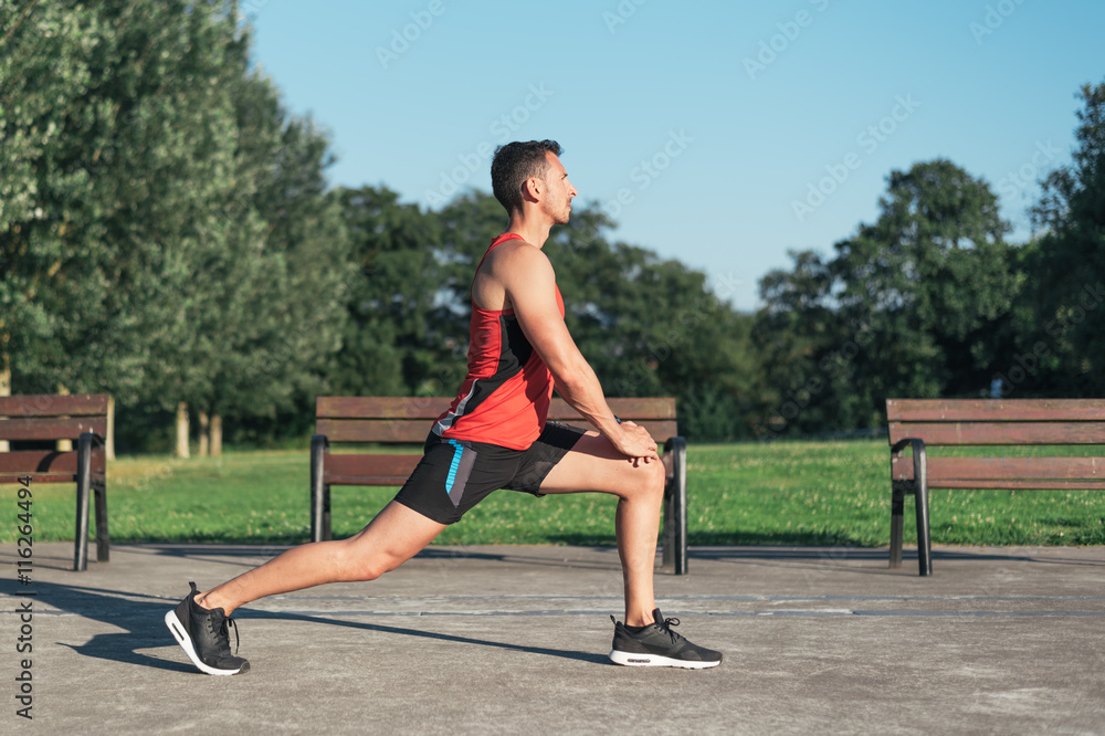 Fitness man stretching legs before outdoor workout. Sporty male athlete in an urban park warming up.