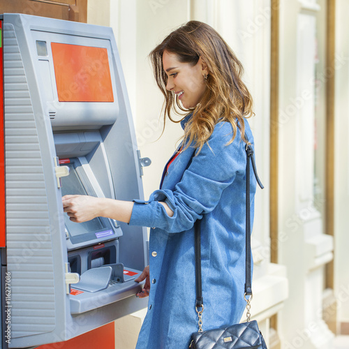 Happy brunette woman withdrawing money from credit card at ATM photo