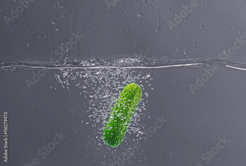 Fresh cucumber falling in water on dark background