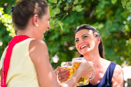 Frauen im Biergarten oder Freisitz sitzen unter Baum und trinken Bier im Schatten, es ist heiß