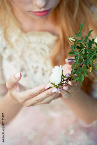 Beautiful girl in a light dress holding a rose on a branch. Tenderness